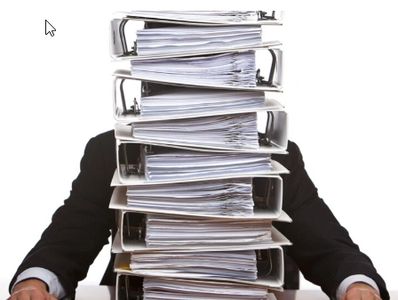 A person sitting behind a large stack of binders full of paper. 