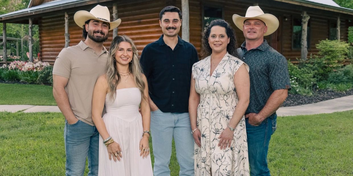 Five people posing outside a log cabin.