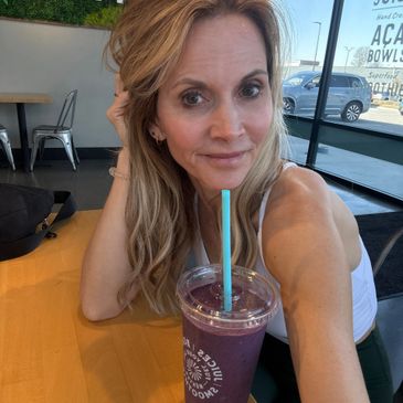 A woman with blonde hair enjoying a purple smoothie at a cafe.