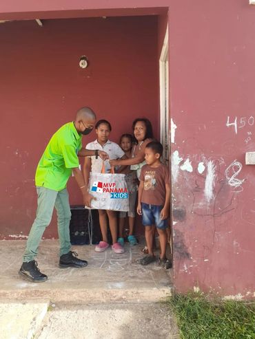 Man in green shirt handing out MVP Panama Kids supplies to children at a doorway.