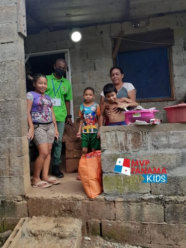 A family with a volunteer outside a concrete house with donated supplies.
