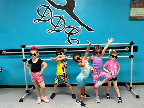Kids in dance attire pose with sunglasses in a studio.