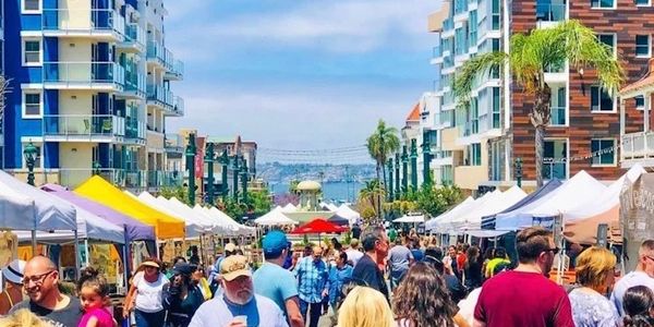 Crowded outdoor market with colorful tents and modern buildings on a sunny day.
