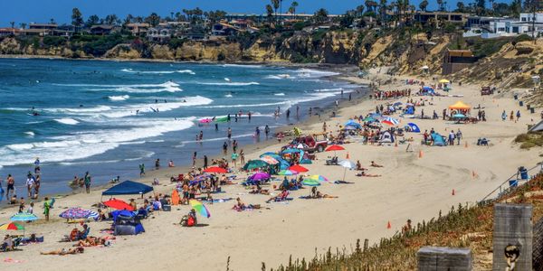 Crowded sunny beach with colorful umbrellas and people enjoying the ocean.