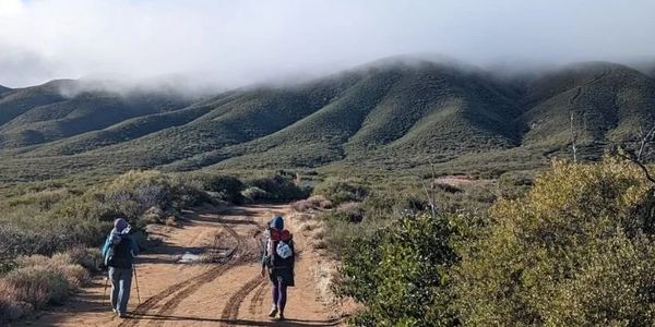 Two hikers walking on a trail towards misty mountains.