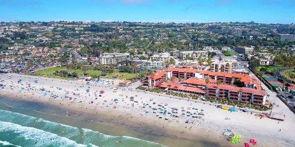 A sunny beach with umbrellas, waves, and a large building near the shore.