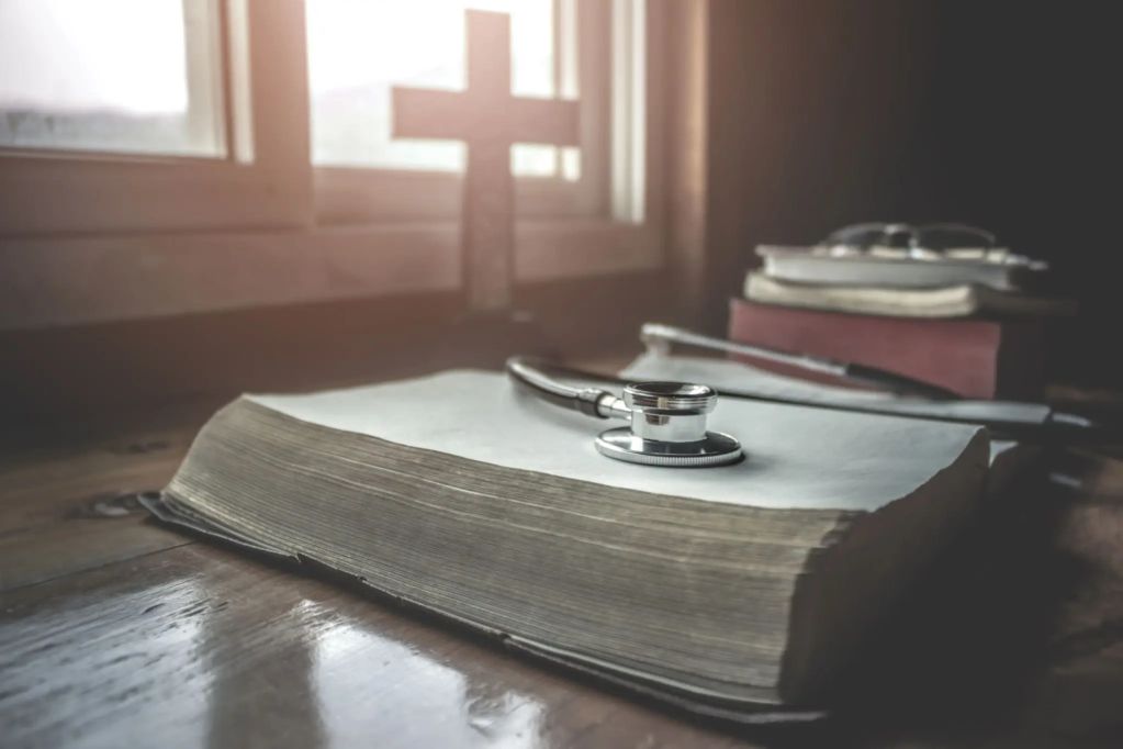 A stethoscope on a thick book with a cross in the background.