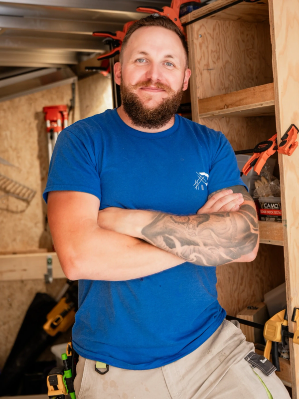 Man with a beard and tattoo smiling in a workshop.