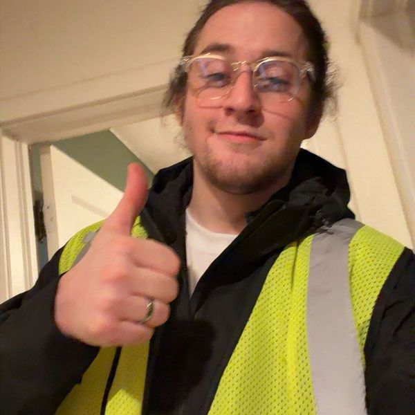 Person in glasses and a safety vest giving a thumbs-up indoors.