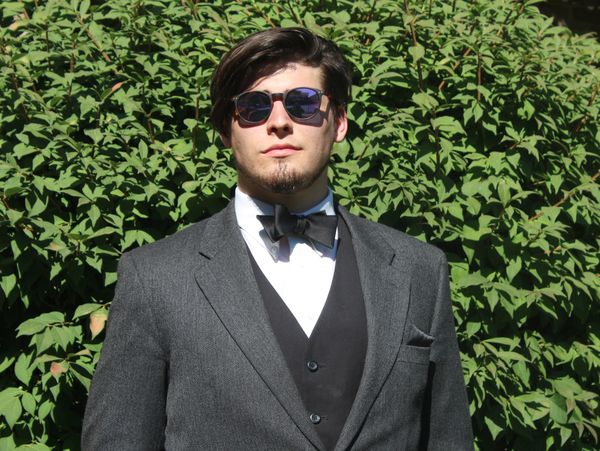 Young man in a suit and sunglasses standing outdoors.