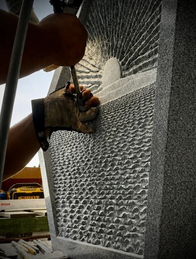 Hand carving a textured stone surface with tools.