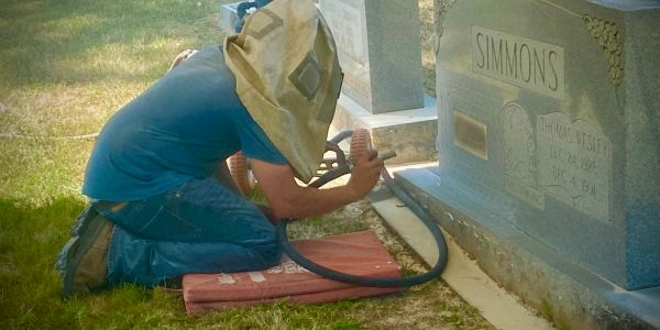 Person wearing protective gear working on a gravestone.