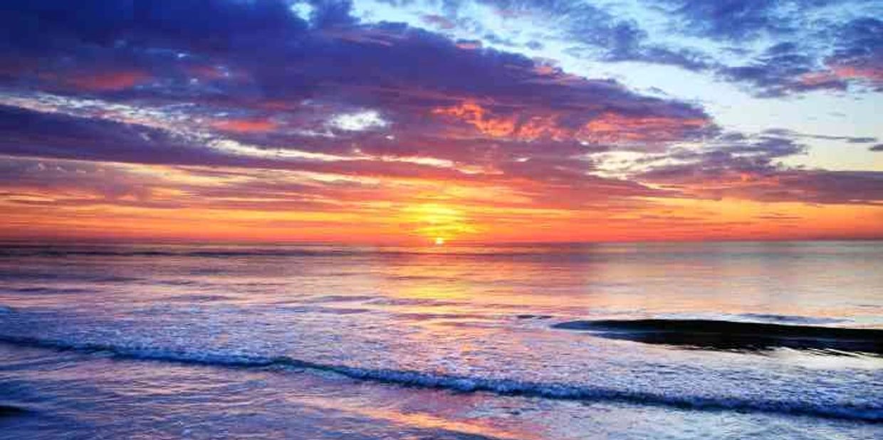 A vibrant sunset over calm ocean waves with colorful clouds.
