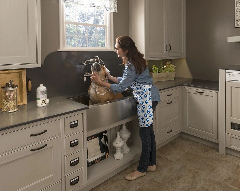 Woman washing a dog in a modern utility room sink.