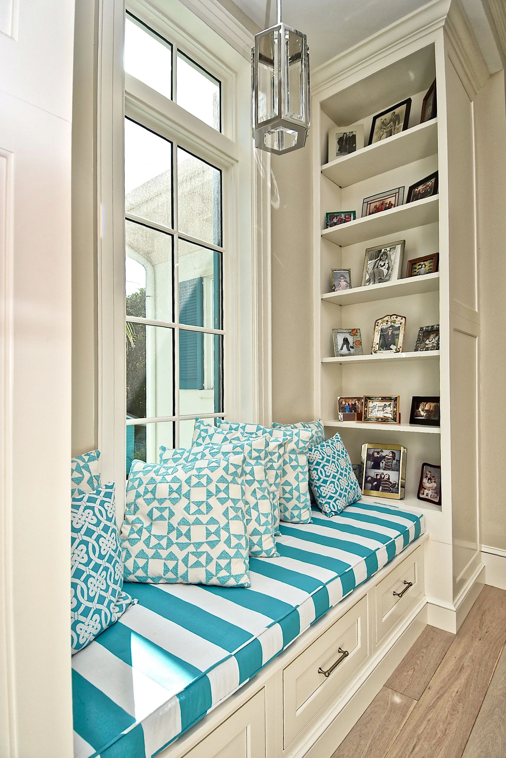 Cozy window seat with blue patterned cushions and family photos on built-in shelves.