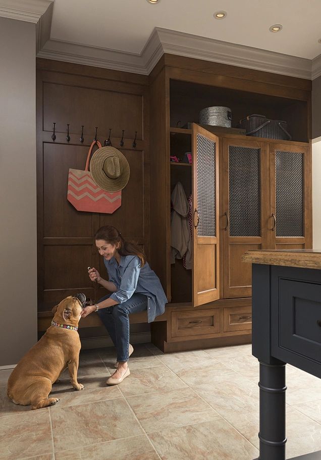 Woman feeding her dog treats in a cozy home entryway with wooden cabinets.