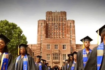 Graduates in caps and gowns stand in front of a historic university building.
