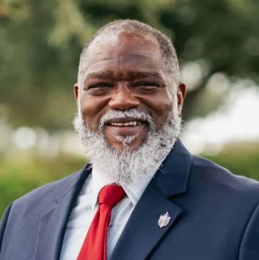Smiling man with white beard in suit and red tie.