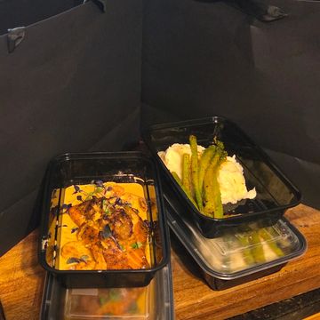 Takeout meals with grilled chicken, mashed potatoes, and asparagus in black containers.