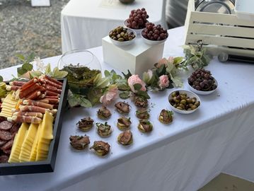 Elegant charcuterie and appetizer display with cheeses, meats, grapes, and olives on a white table.