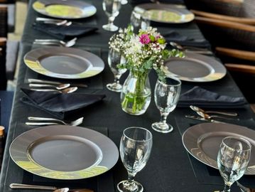 Elegantly set dining table with black tablecloth and floral centerpieces.