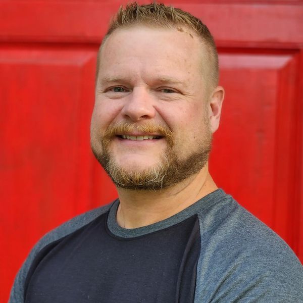 Smiling man with beard in front of a bright red background.