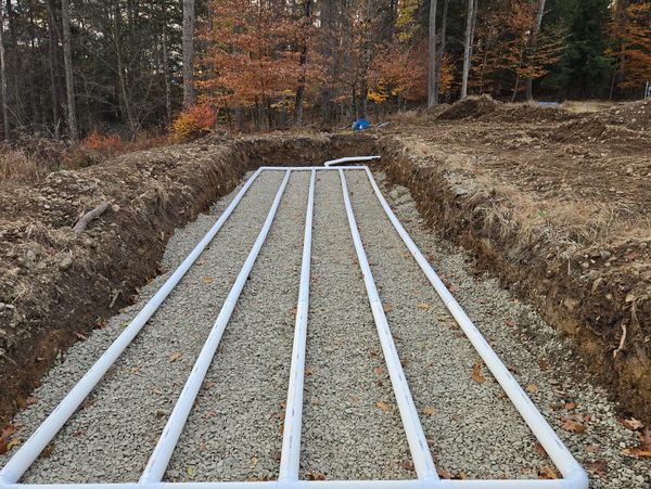 PVC piping laid in a trench filled with gravel, surrounded by autumn trees.