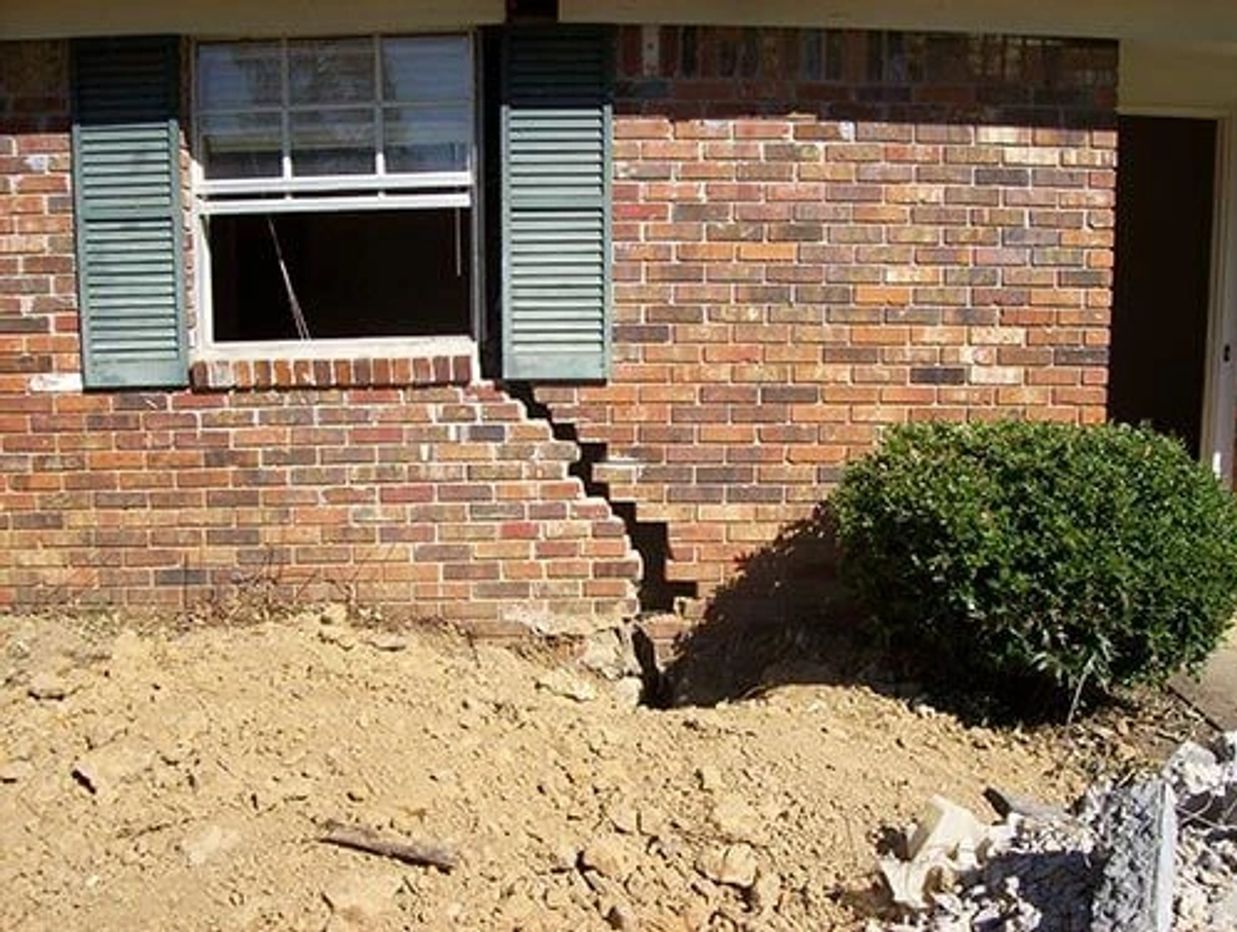 Huge structural damage crack in a brick wall of a house with dirt in the yard