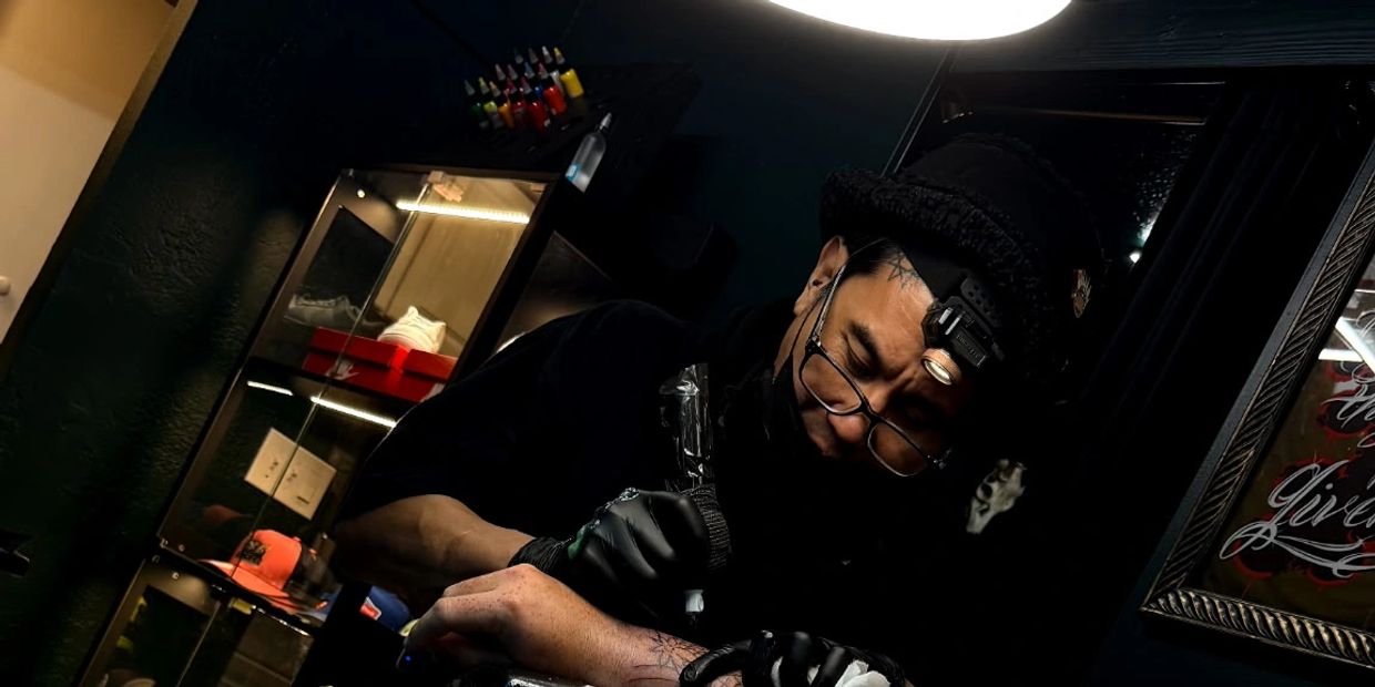Tattoo artist focused on creating a detailed tattoo in a dimly lit studio.