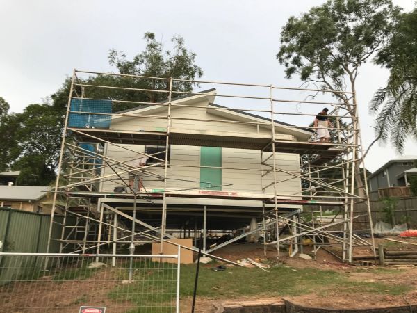 House under construction with scaffolding around it and workers on site.
