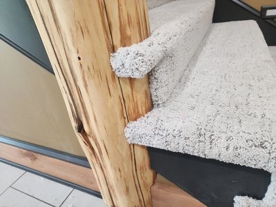 Carpeted stairs with a wooden post and carpet edges extending beyond the steps.