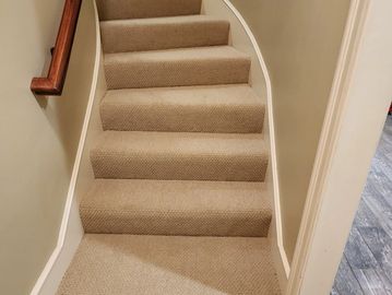 Narrow carpeted staircase with beige carpeting and wooden handrail. Installed by Flooring it KC 