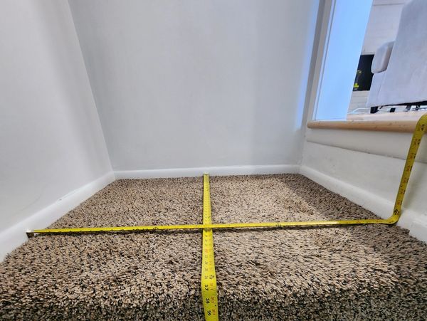 Two yellow measuring tapes crossing on carpeted stairs against a white wall.