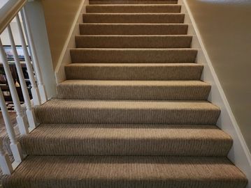 Carpeted indoor staircase with beige walls and white railing. Installed by Flooring it Kc 
