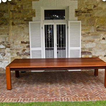 Wooden table under a covered patio in front of a stone wall.
