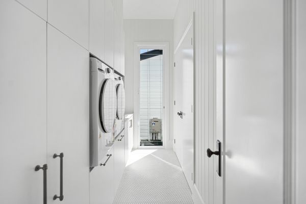 Narrow laundry room with white walls and appliances.