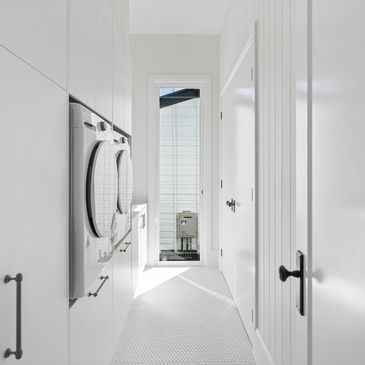 Narrow laundry room with white walls and appliances.