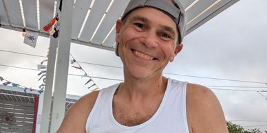 Smiling man in a tank top and backwards cap.