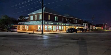 Corner building lit up at night with parked cars.