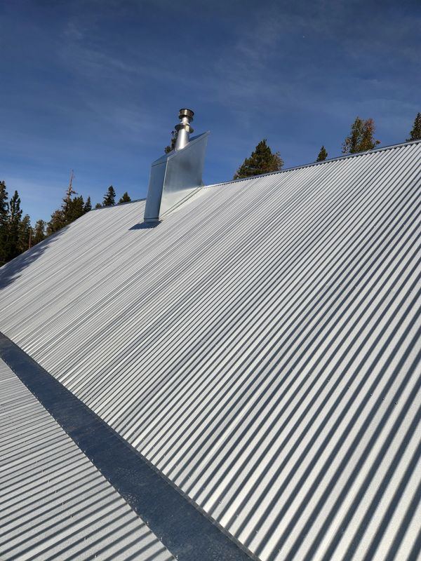 Corrugated metal roof with a chimney under a clear blue sky.