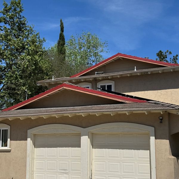 House with beige walls, red roof edges, and white garage doors under a clear blue sky.