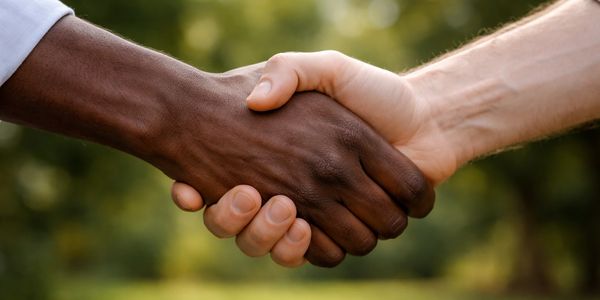 Two hands, one dark-skinned and one light-skinned, shaking in unity.