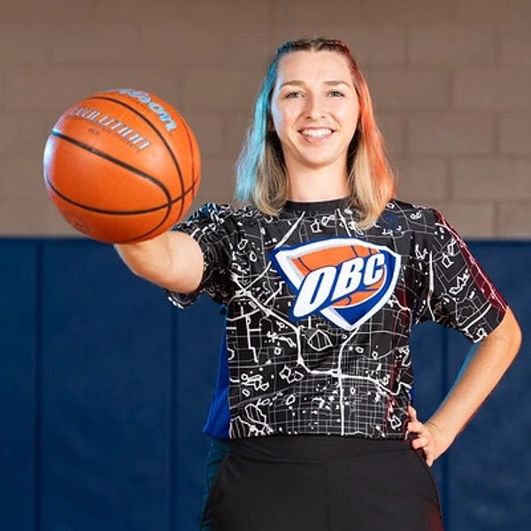 Smiling woman holding a basketball in a gym.