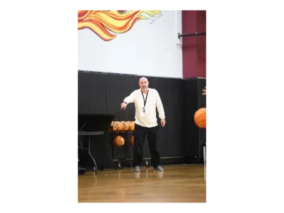Coach standing in gym with basketballs and a whistle.