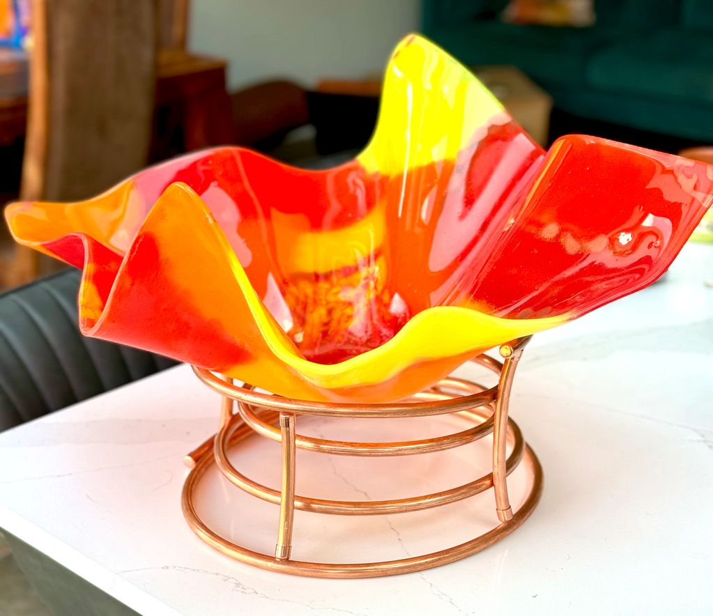 A large custom made glass bowl set on a copper stand - bright reds, oranges and yellow