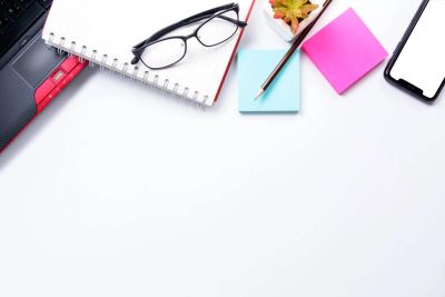 Desk setup with glasses, notebook, sticky notes, plant, and smartphone.