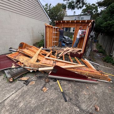 Two men dismantle a small wooden shed with debris scattered around.