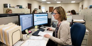 Woman working at a desk with dual monitors in an office.
