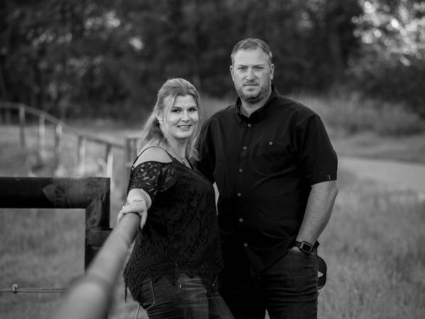 Couple posing outdoors near a fence.