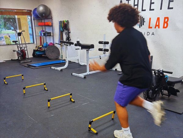 Person performing agility drills over hurdles in a gym.